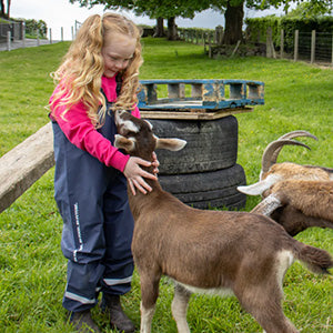 Girl wearing Grassmen branded waterproofs, talking to a goat.